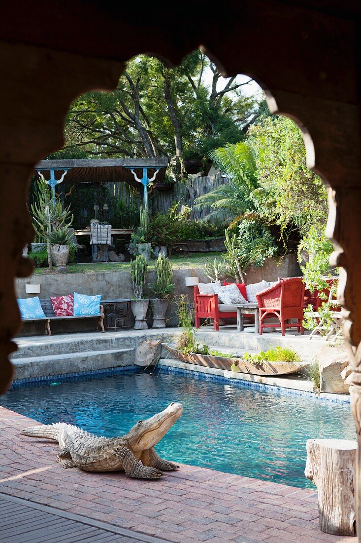 Blick durch geschnitzten Holz Rundbogen auf Pool mit Krokodil-Figur am Poolrand