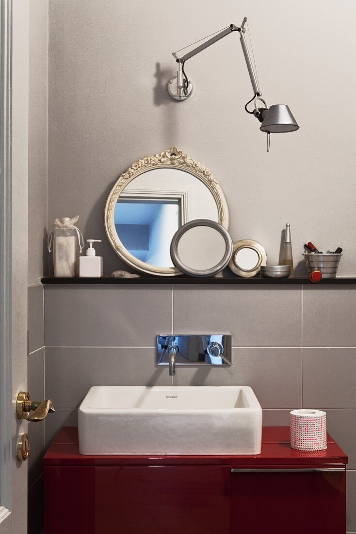 Waschtisch mit Trogbecken auf rotem Unterschrank unter Designer Wandleuchte und Sammlung runder Spiegel
