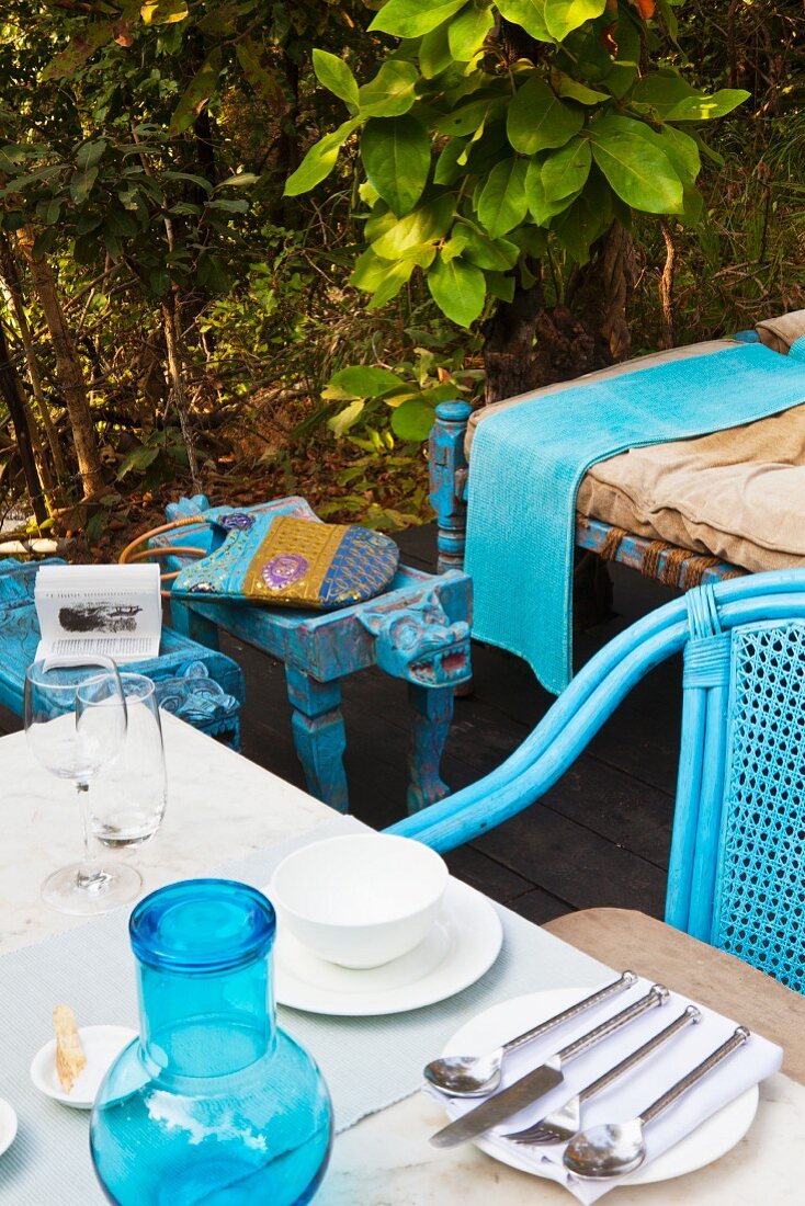 Gedeck mit Besteck auf Tisch und blauer Outdoor Stuhl auf Terrasse in Freiem