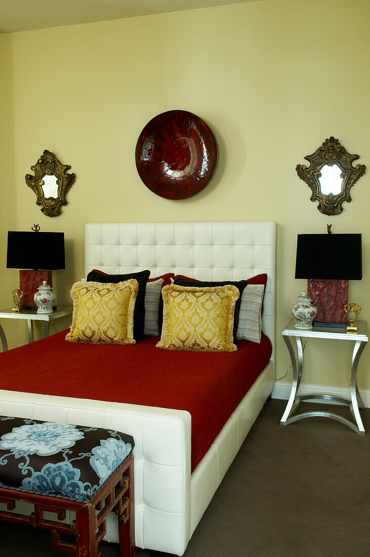 Classic sleigh bed with white upholstered frame flanked by bedside tables against yellow-painted wall in bedroom with Oriental atmosphere