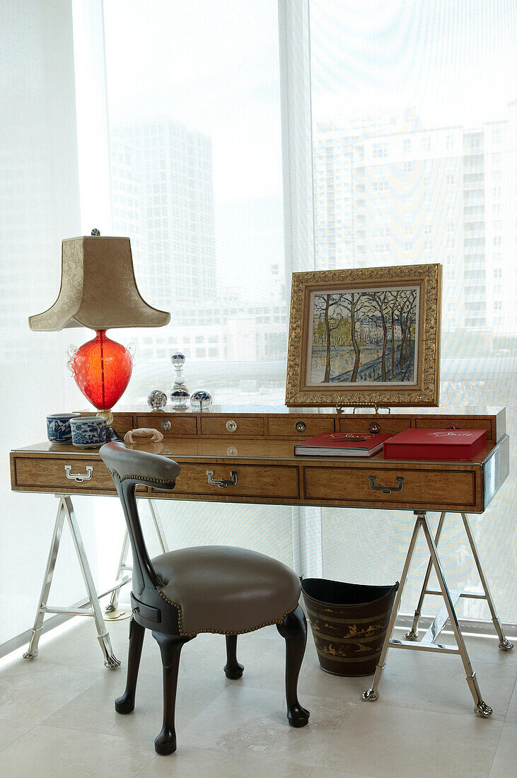 Desk with antique handle fittings on stylised, chrome trestles and upholstered leather chair in front of glass wall