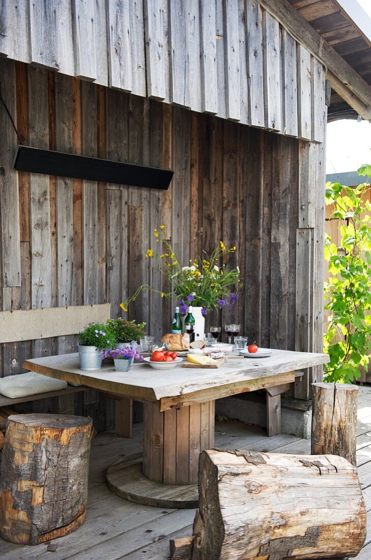 Table with bench and tree stump stools on terrace of wooden cabin