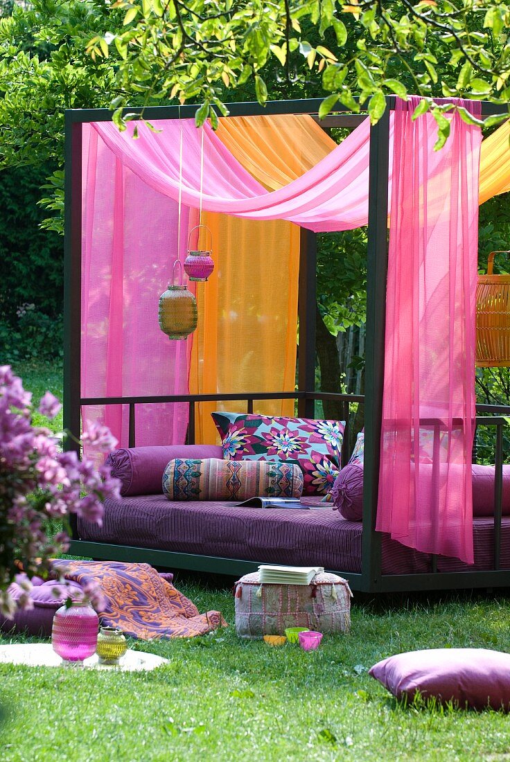 Exotischer Farbklang im Garten - Modernes Tagesbett aus Metall mit gemusterten Kissen und Baldachin aus duftigen Tüchern