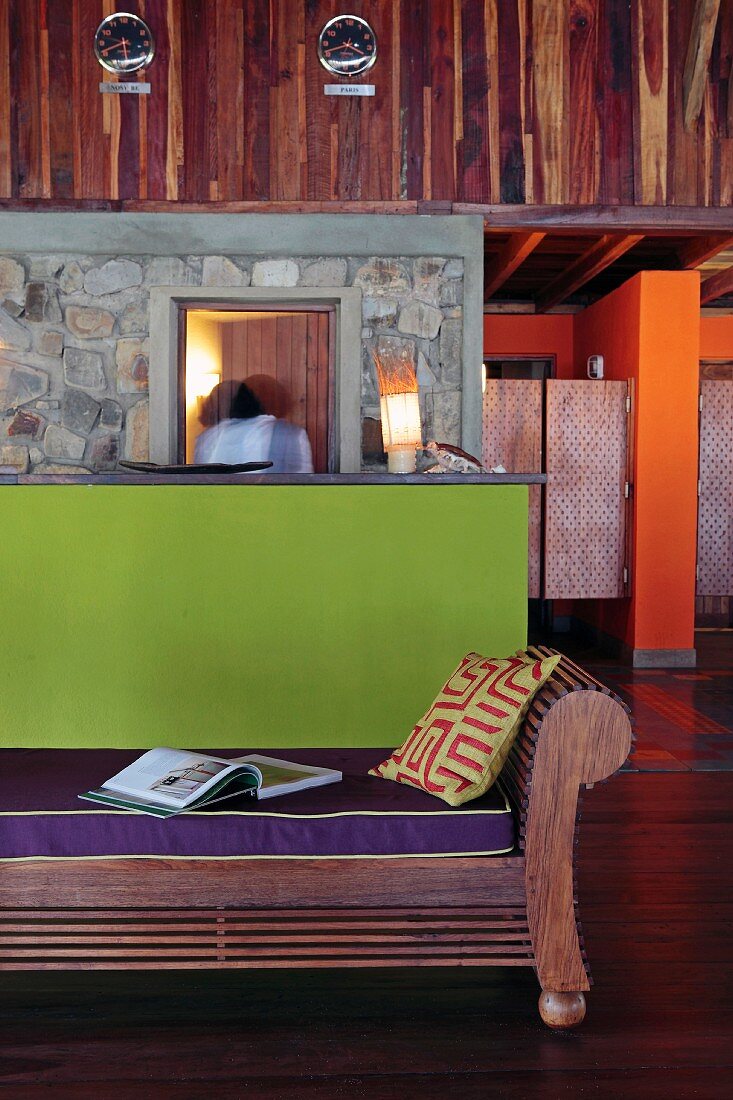 Farbkontraste im Empfangsbereich einer Öko-Lodge; Wandverkleidung und dekorative Holzbank aus afrikanischem Edelholz