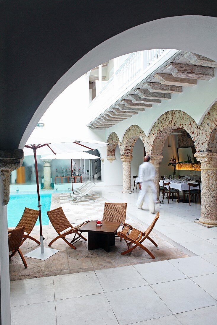 Blick durch Rundbogen auf Pool und Outdoor-Möbel in orientalischem Innenhof eines Hotels