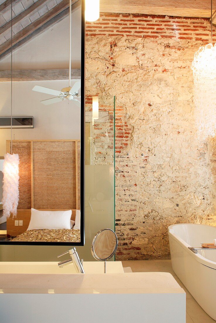 Designer bathroom furnishings, rustic brick wall and view of bed reflected in mirror
