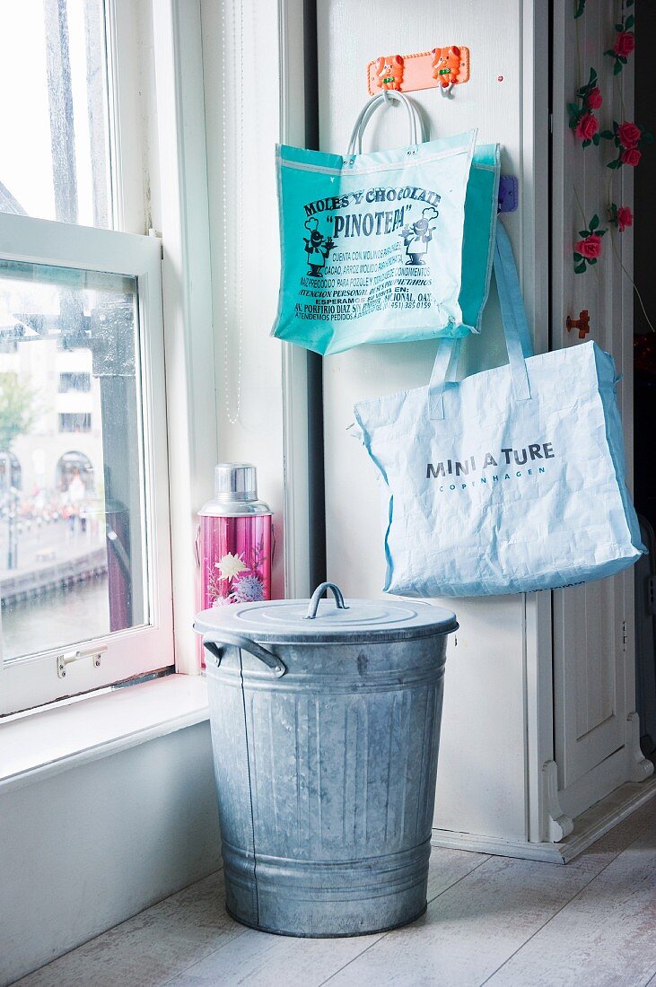 Zinkeimer mit Deckel und bedruckte Taschen in Küche neben Schiebefenster