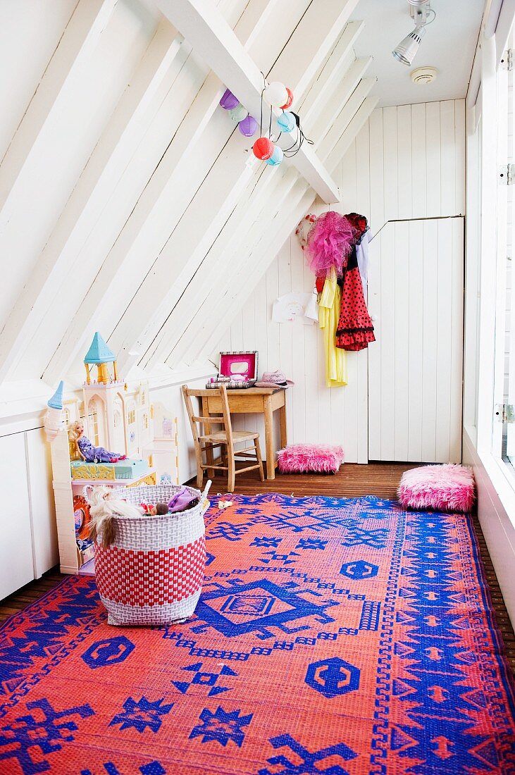 Weiß lackiertes Holz und rotblauer Kelim in Mädchenspielzimmer unter schrägem Dach