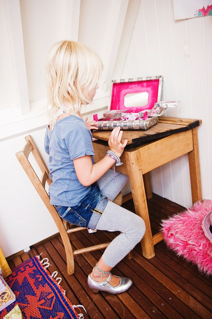 Little girl looking into open jewellery box with mirror on wooden table