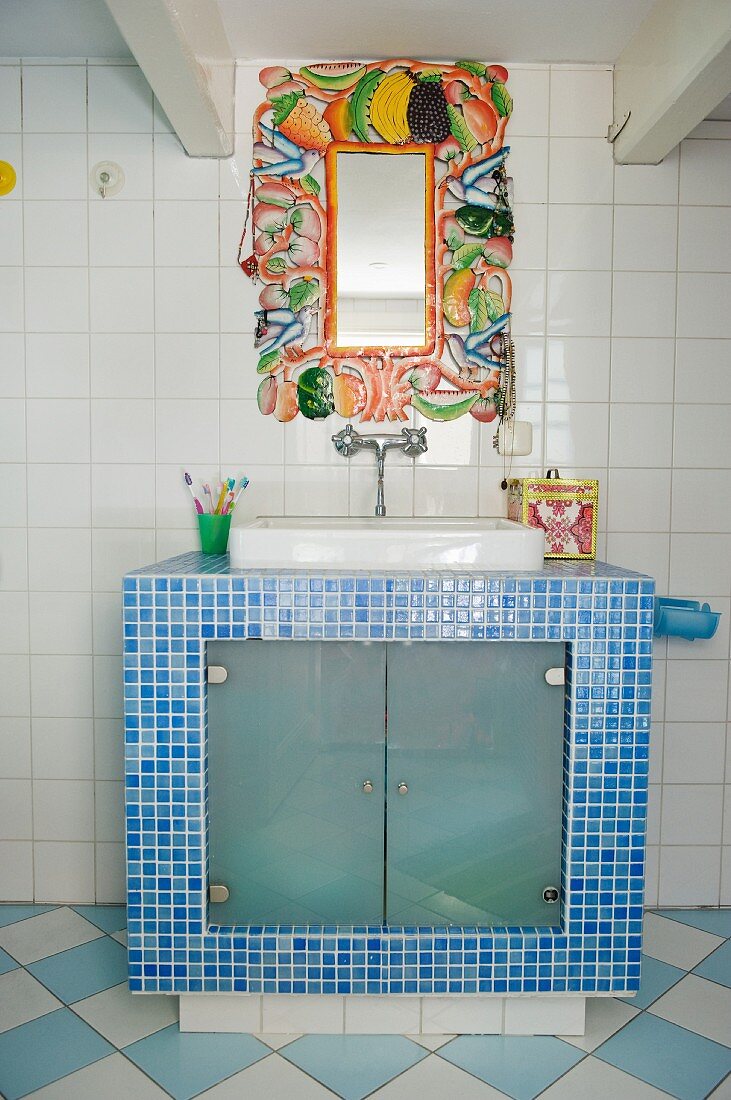 Mirror frame with vegetable motifs above masonry washstand with blue mosaic tiles