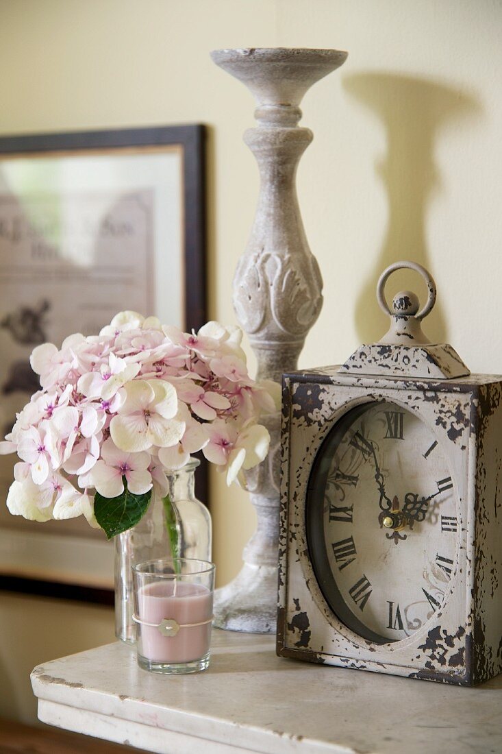Antike Tischuhr, Kerzenständer, Hortensienblüte und Duftkerze auf einer Ablage