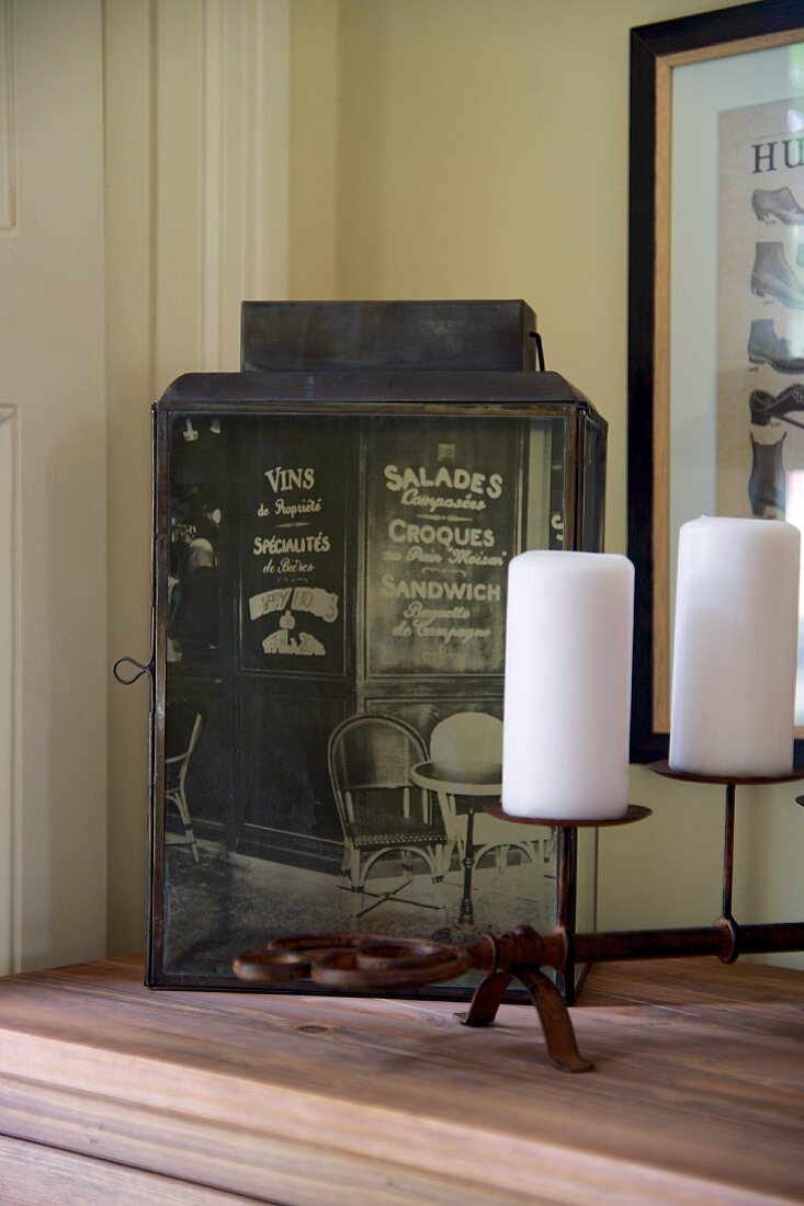 Antique lantern covered with printed photo motif and white pillar candles on candlesticks