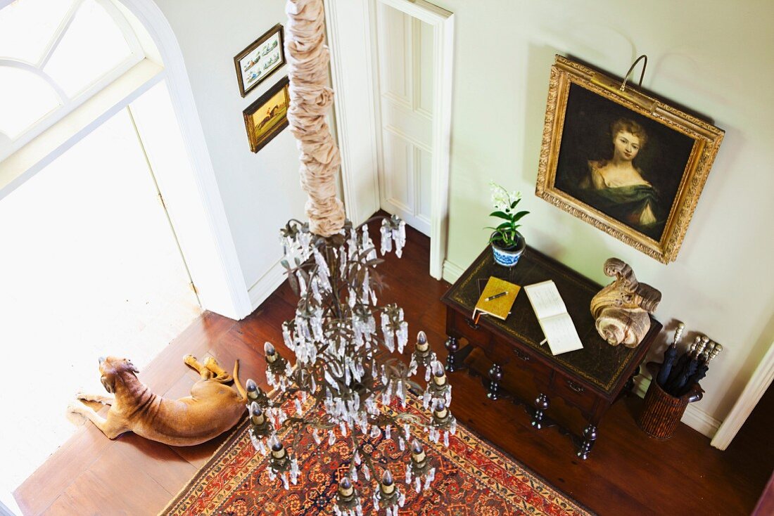 Blick von oben in herrschaftliches Foyer - Kronleuchter über Orientteppich und antiker Wandtisch vor Ölgemälde