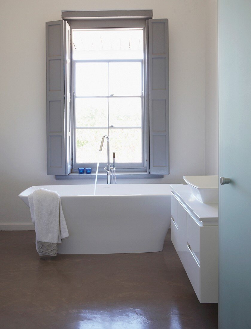 View through open door into designer bathroom with free-standing bathtub below window