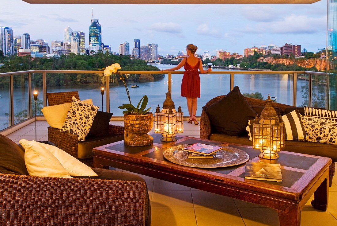 Lounge armchairs and lanterns on opium table on terrace with view of river and Brisbane skyline