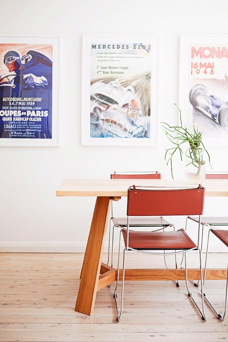 Filigraner Metallstuhl mit Leder Sitzfläche und Rückenlehne an Holztisch vor Wand mit gerahmten Postern