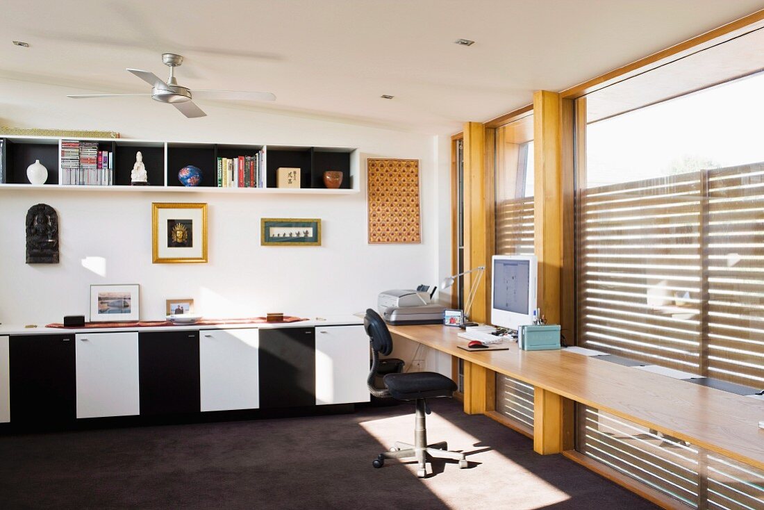 Geräumiges Home Office mit Schreibplatte vor Fensterfront; Bilder und Skulpturen über Sideboard mit Schwarzweiss Fronten
