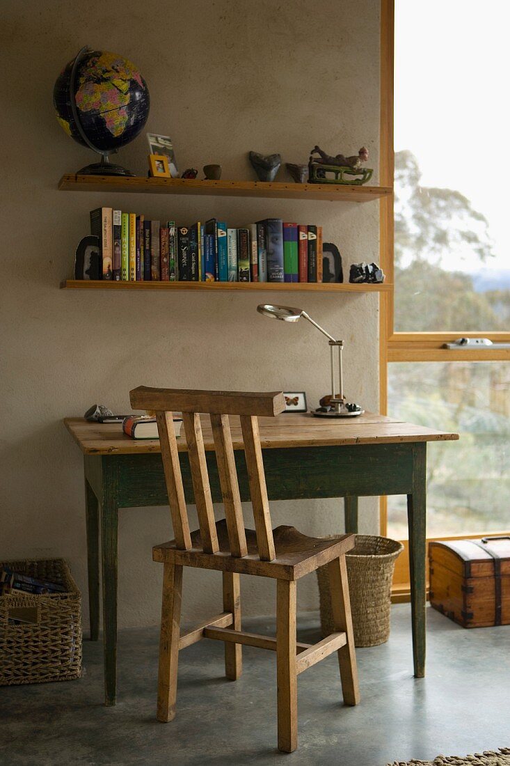 Rustic wooden chair and table in front of a concrete wall and book shelves next to a floor to ceiling window with a view