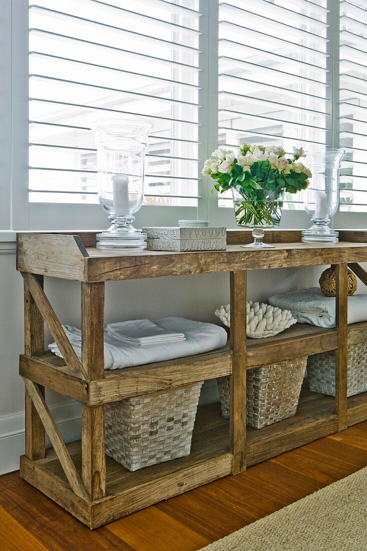Storage baskets and fresh laundry below rustic wooden table; elegant candle lanterns and bouquet of white summer flowers on table top