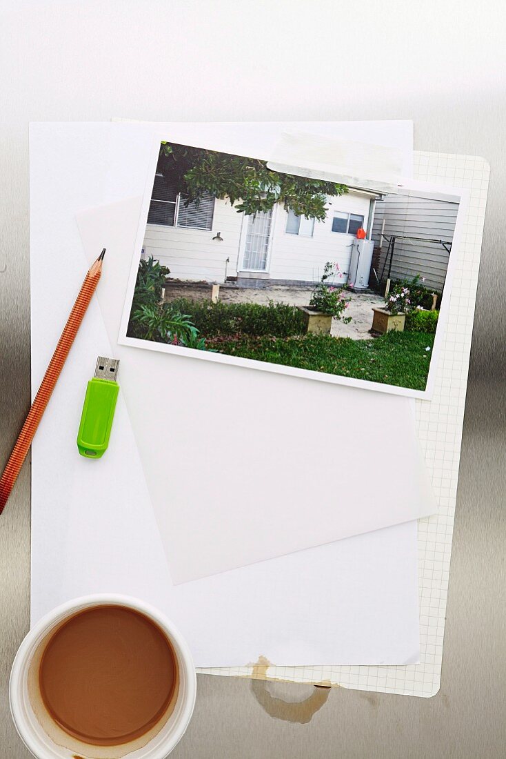 Foto von einem Haus neben Bleistift, Computerstick & Tasse Kaffee auf Blatt Papier