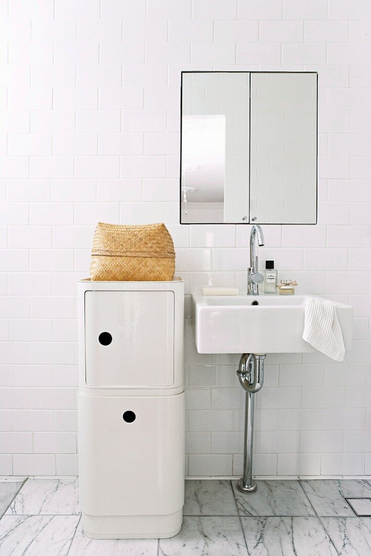 Halbhoher Designer Aufbewahrungsmöbel in Weiß neben minimalistischem Waschtisch vor weisser Fliesenwand und eingebautem Spiegelschrank