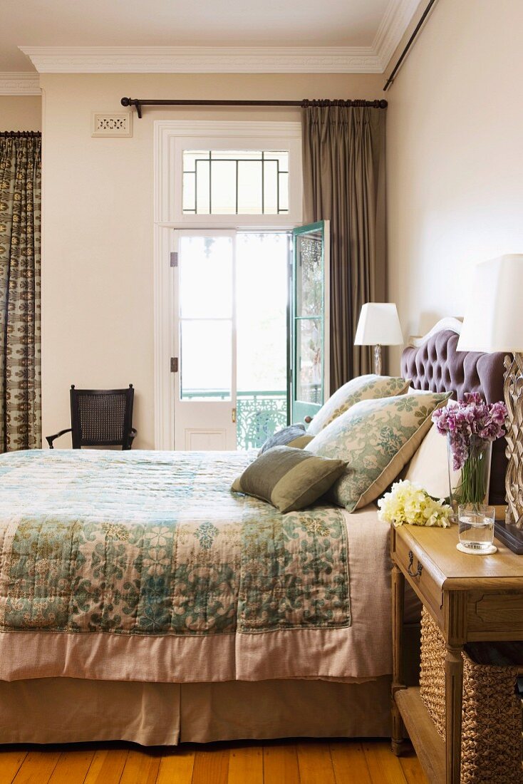Doppelbett mit eleganter Tagesdecke und passenden Kissen neben offener Balkontür in traditionellem elegantem Schlafzimmer