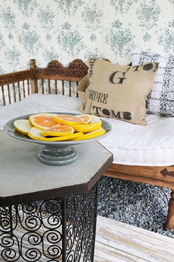 Schale mit Zitrusfrüchte auf Tisch und Holz Sitzbank mit Schnitzereien in Rückenlehne vor Wand mit geblümter Stofftapete