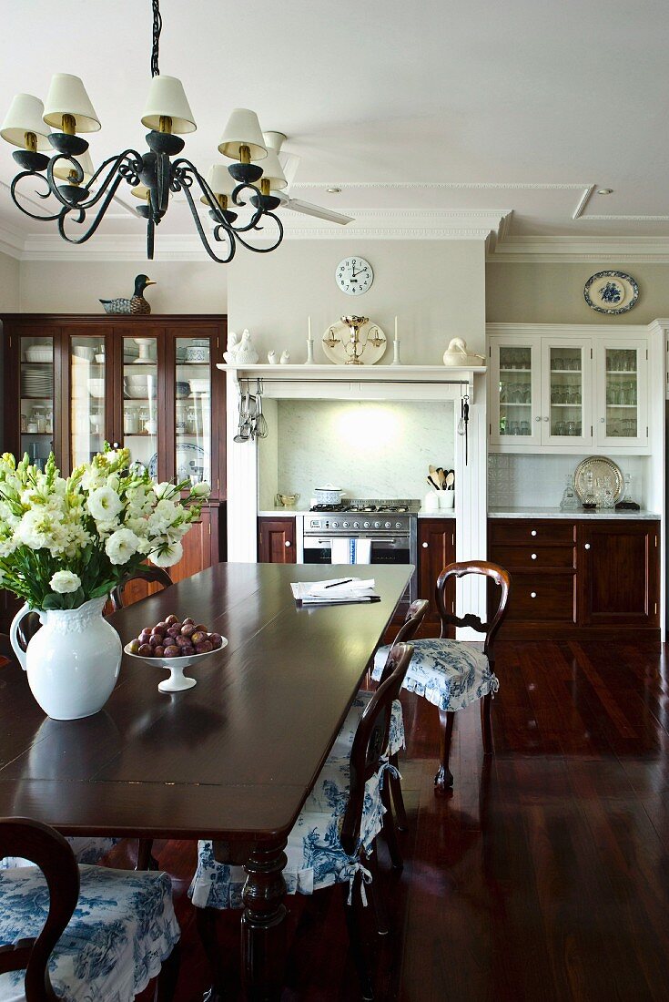 Long dining table and wooden chairs with ruched chair cushions in a open living room with a dignified and luxurious built-in kitchen