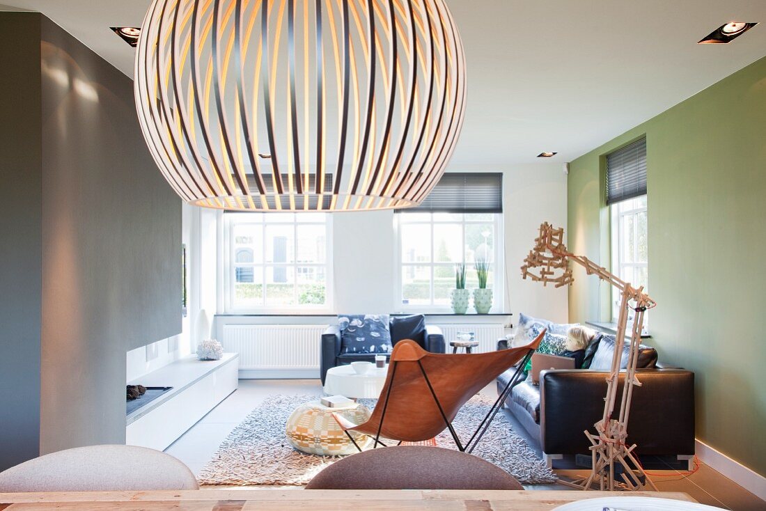 Designer Hängeleuchte aus Holzlamellen in minimalistischem Wohnraum mit Butterfly Sessel und Ledersofagarnitur