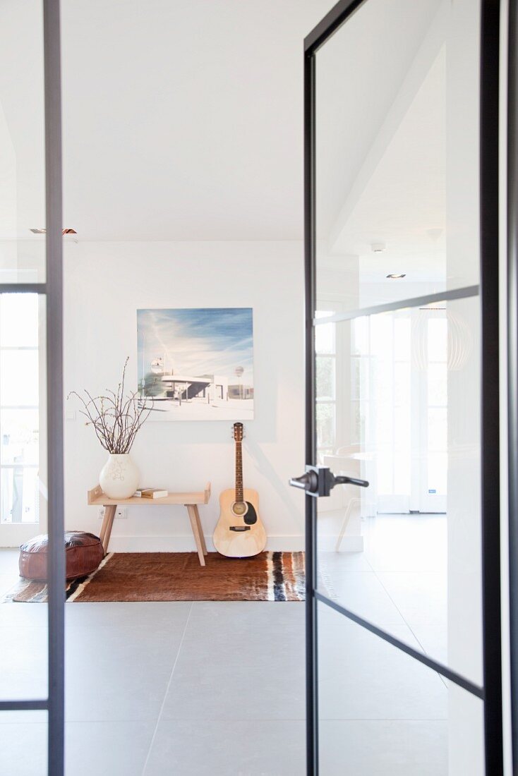 View of vase of flowers on side table, guitar and picture on wall through open glass door with delicate metal frame