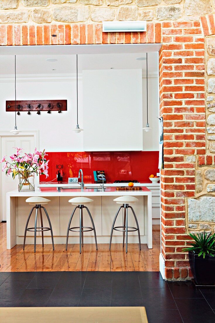 View though wide open doorway in brick wall of designer barstools at counter in open-plan fitted kitchen
