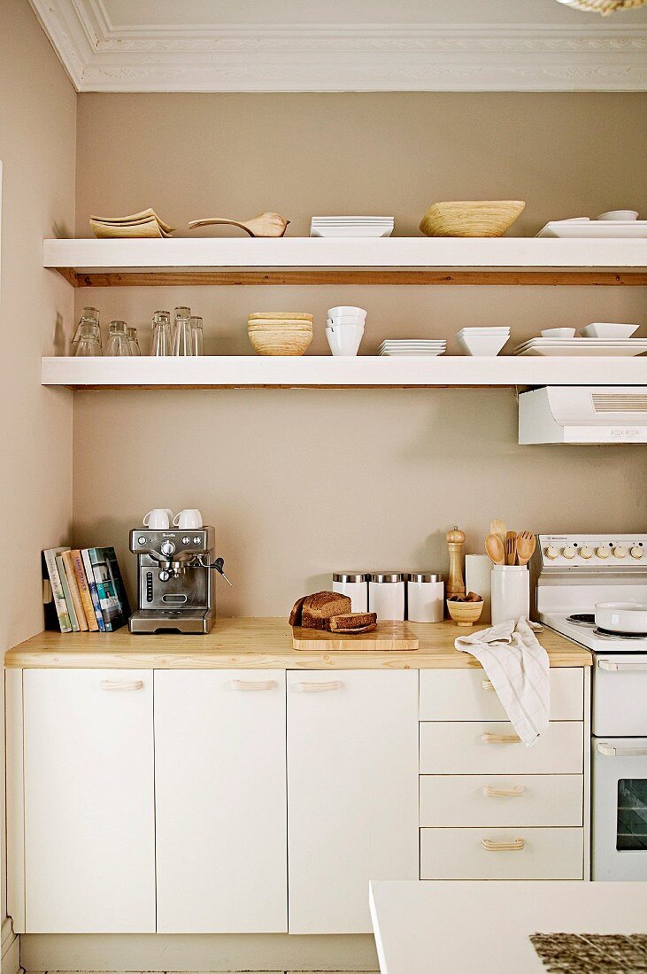 Fitted kitchen with white base units and white floating shelves against beige-painted wall in traditional interior