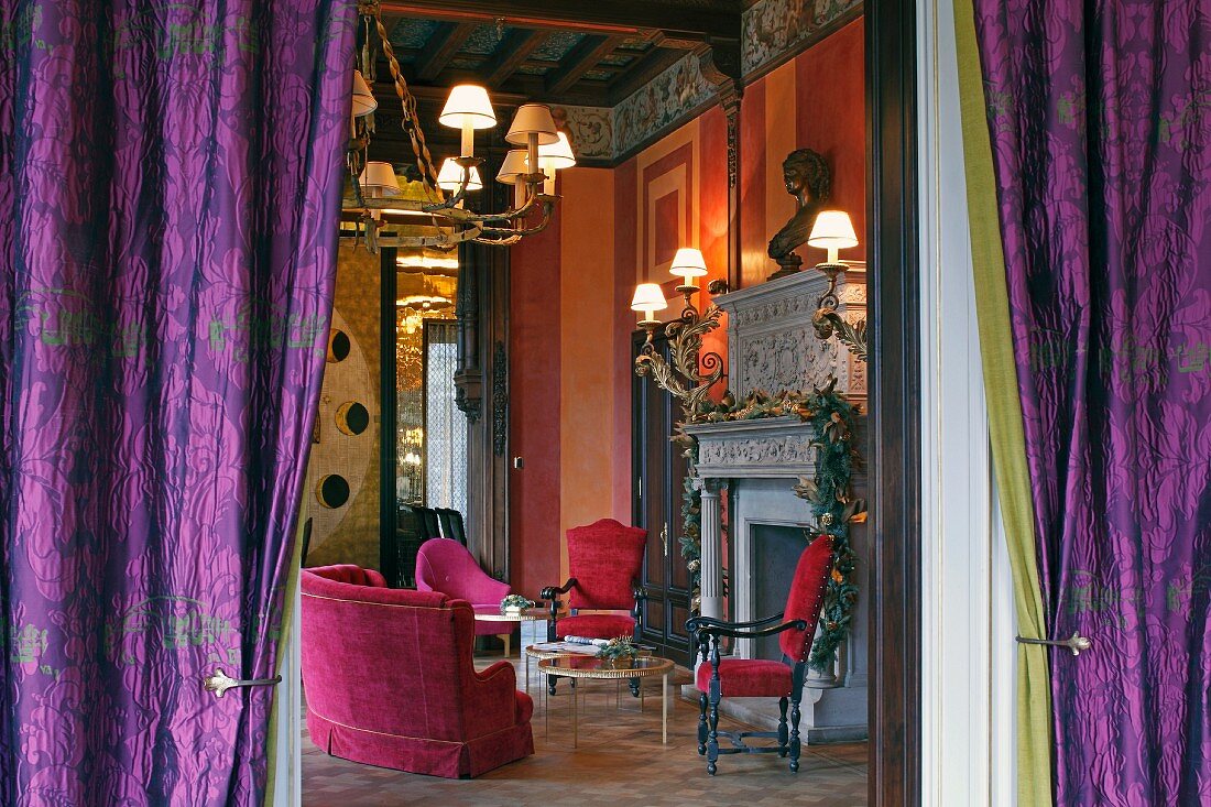 Blick durch violette Vorhänge in prunkvollen Renaissance Salon mit roten Polstermöbeln vor dem Kamin