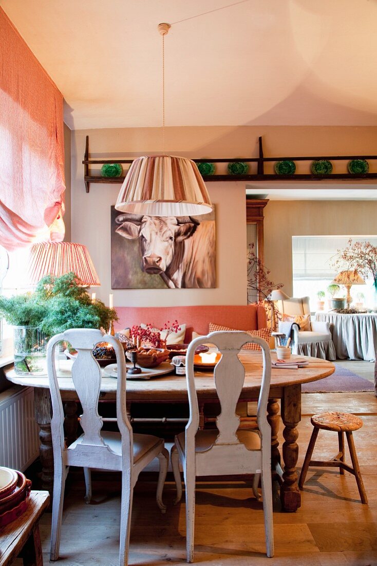 Rustic dining table below window; portrait of cow above sofa in background