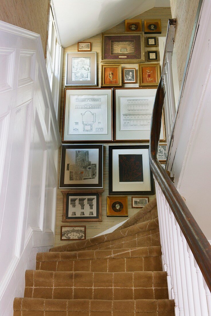 Blick von unten auf traditionellen Treppenaufgang mit Teppichbelag und gerahmten Bildern an Wand