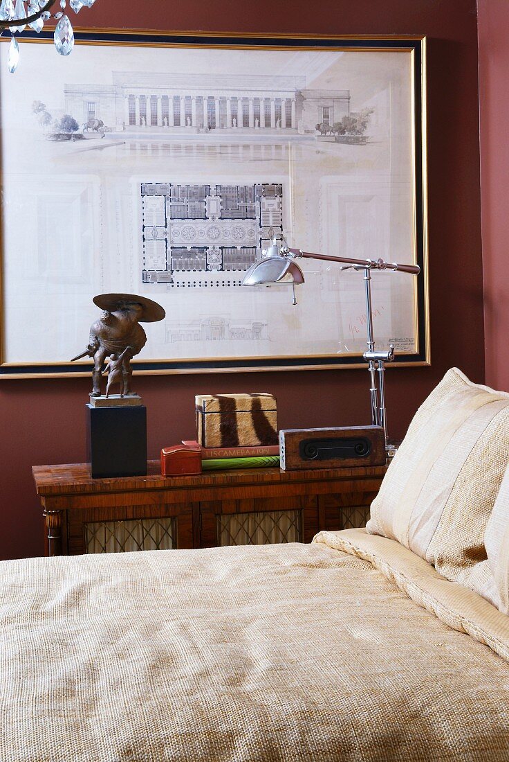 Bett mit Leinenbettwäsche in Naturfarben vor Retro Stehleuchte und gerahmte Architekturzeichnung an dunkelroter Wand