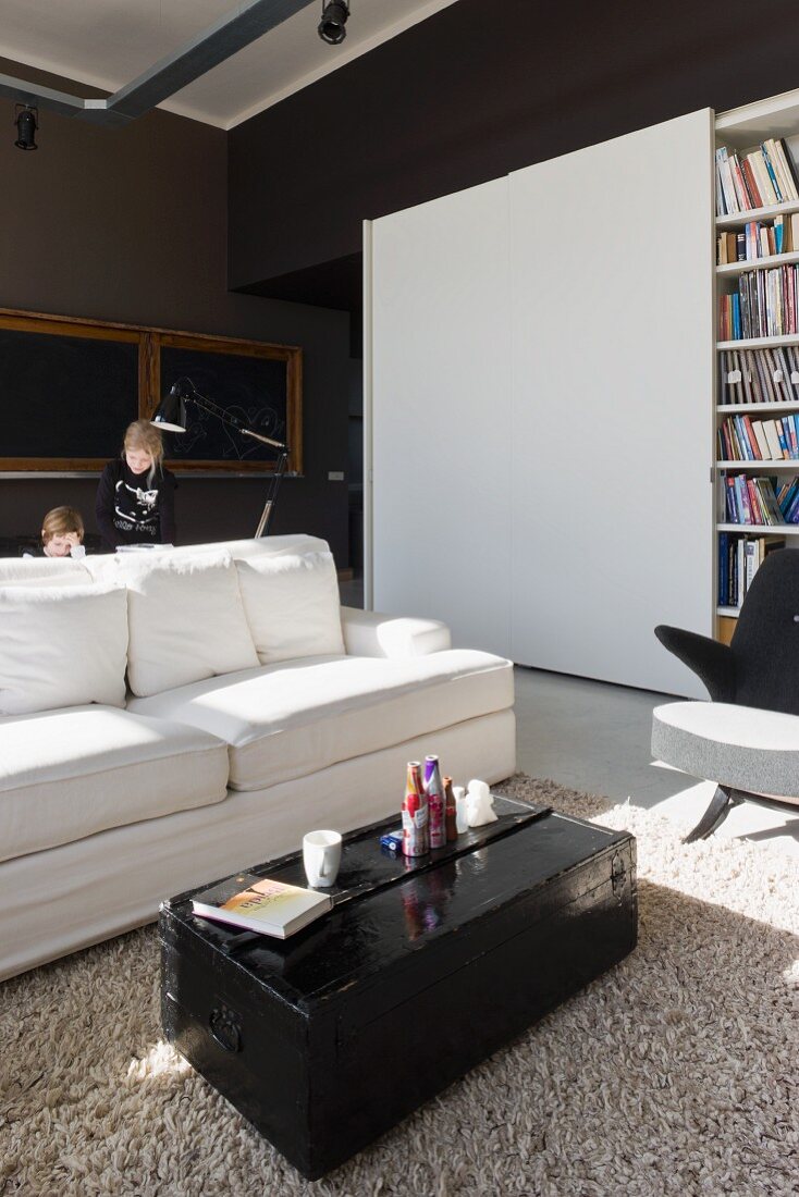 Sunny interior with black-painted travelling trunk as coffee table in front of white sofa