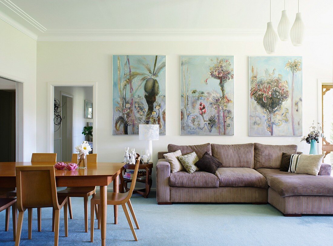Essplatz mit Holzstühlen im Retro Stil und Polstercouch an Wand unter Bildern mit Blumenmotiv in Wohnzimmer mit umlaufendem Stuckfries an Decke