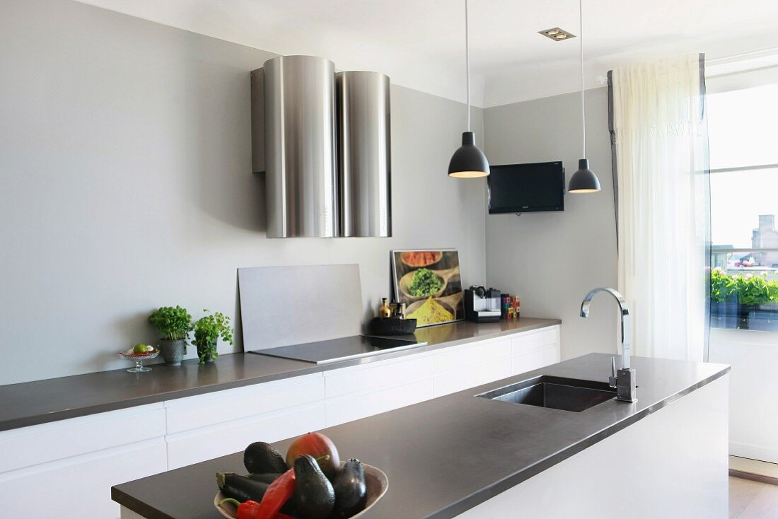 Freistehender Küchenblock mit eingebauter Spüle unter Hängeleuchten und Küchenzeile an Wand mit futuristischem Dunstabzug