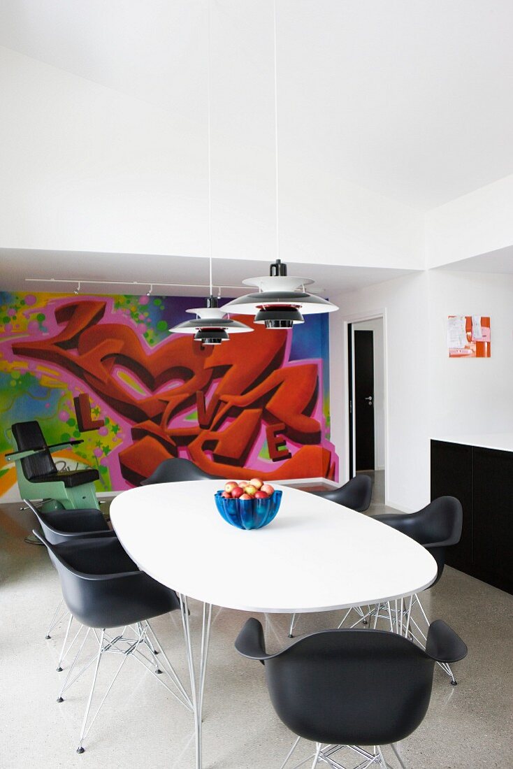 Classic, black shell chairs and table with white top in front of graffito mural on wall of modern interior