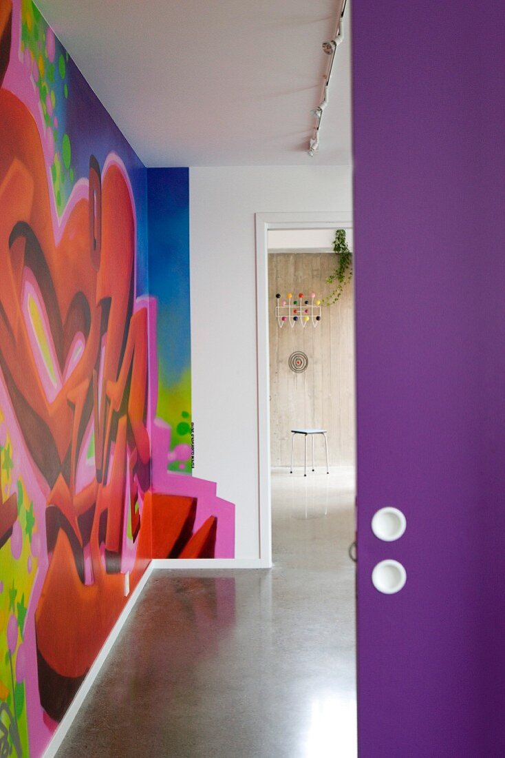 View through open purple door into modern hall with colourful graffito mural
