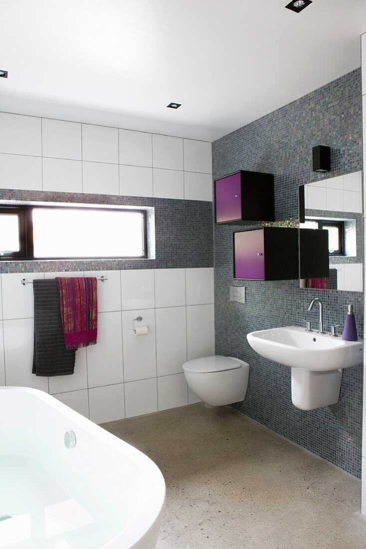 Waschbecken und kleine farbige Schränkchen an der Wand mit grauen Mosaikfliesen