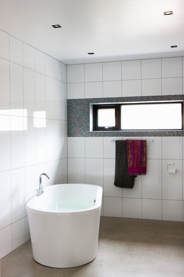 Modernes Bad mit freistehender Badewanne vor Wand mit weissen Fliesen und Oberlichtband
