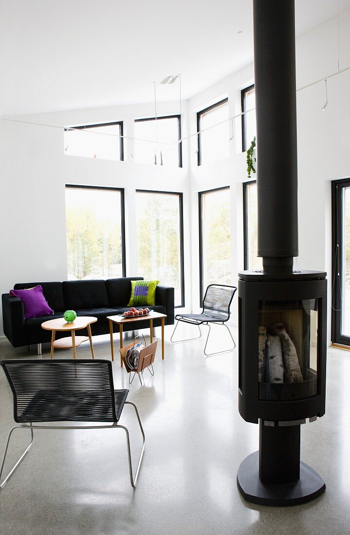Free-standing log burner next to modern Spaghetti chair in open-plan interior with lounge area in eclectic mix of styles