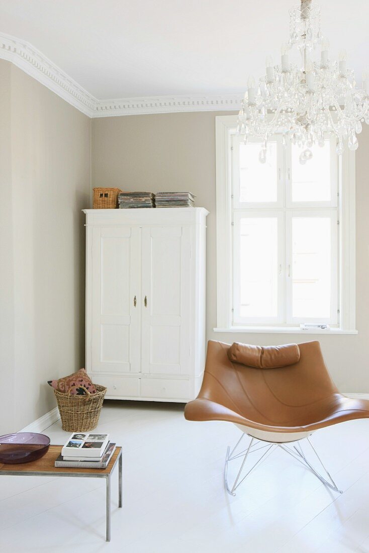 Moderner Sessel unter Kronleuchter und weiss lackierter Bauernschrank in renoviertem Wohnraum