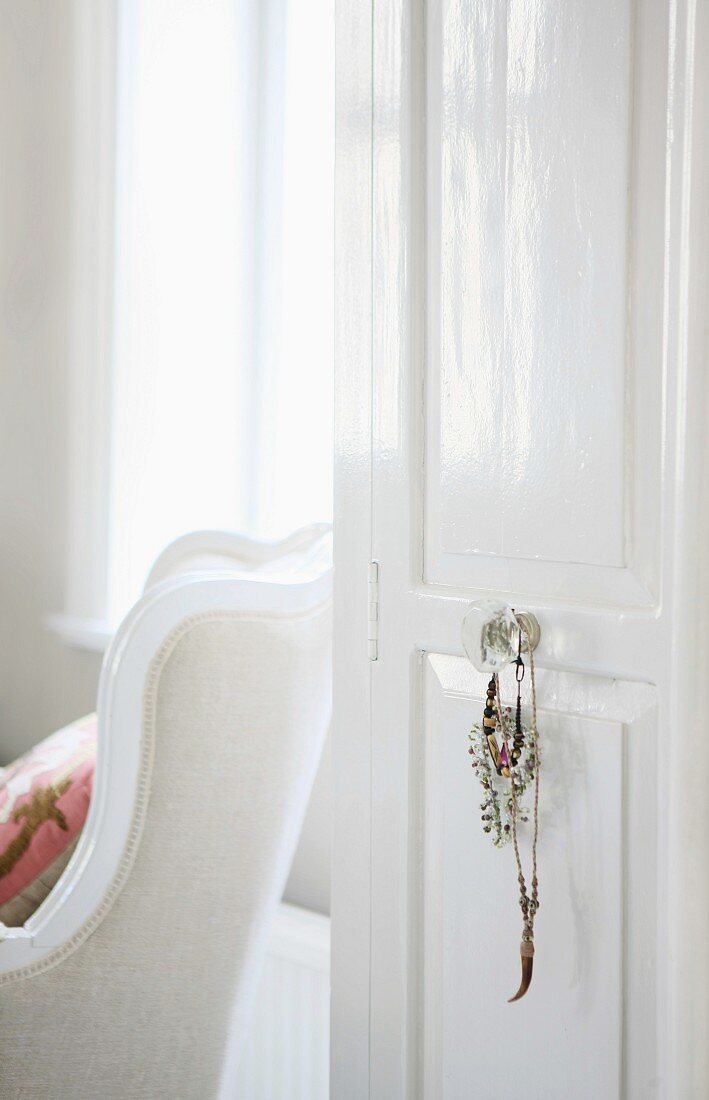 Offene weiss lackierte Zimmertür mit Dekoschmuck am Griff gehängt und Blick auf traditionellen Sessel