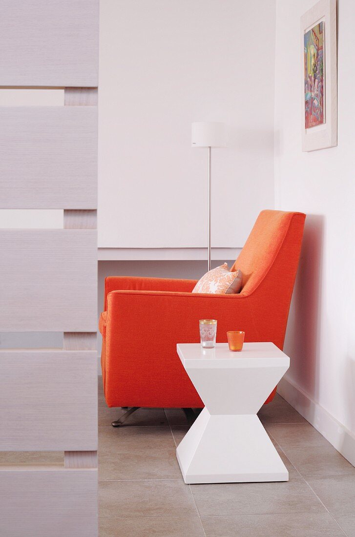 Sitzecke mit skulpturalem Beistelltisch aus Kunststoff und orangefarbenem Polstersessel