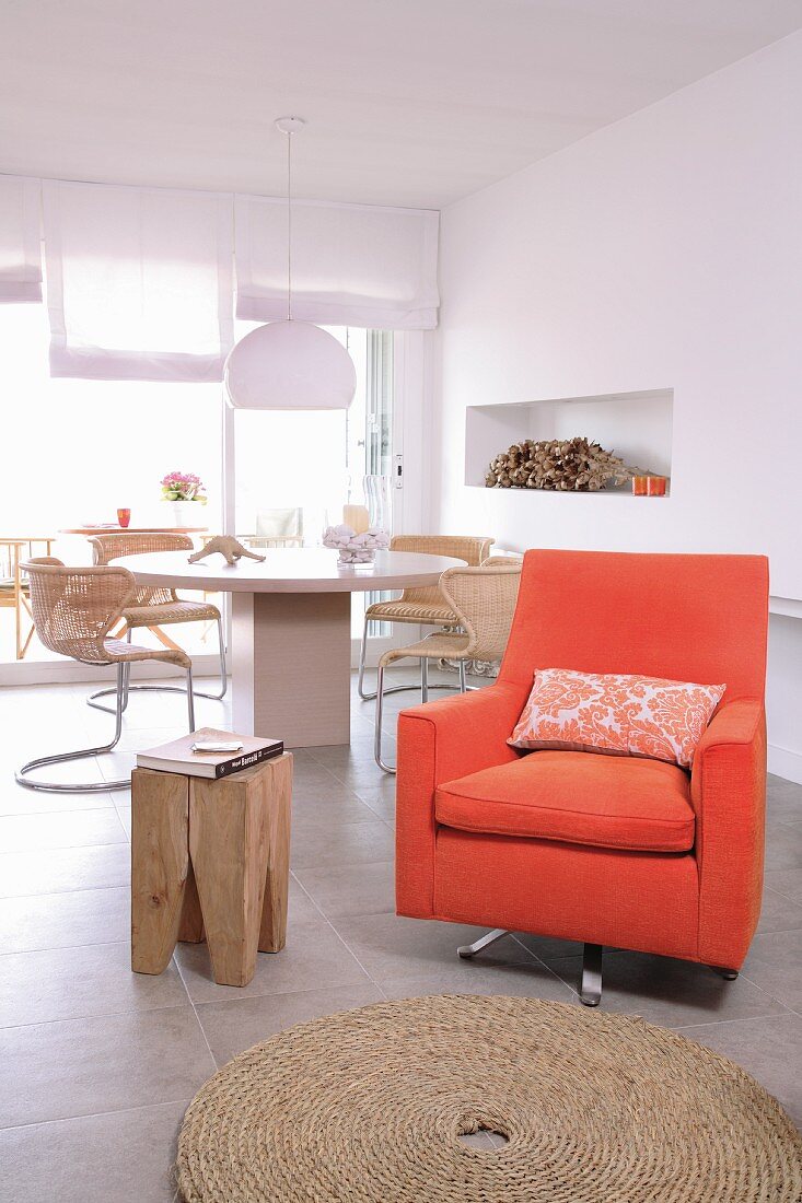 Orangefarbener Sessel und Designerhocker aus Holz vor rundem Essplatz mit Freischwingerstühlen