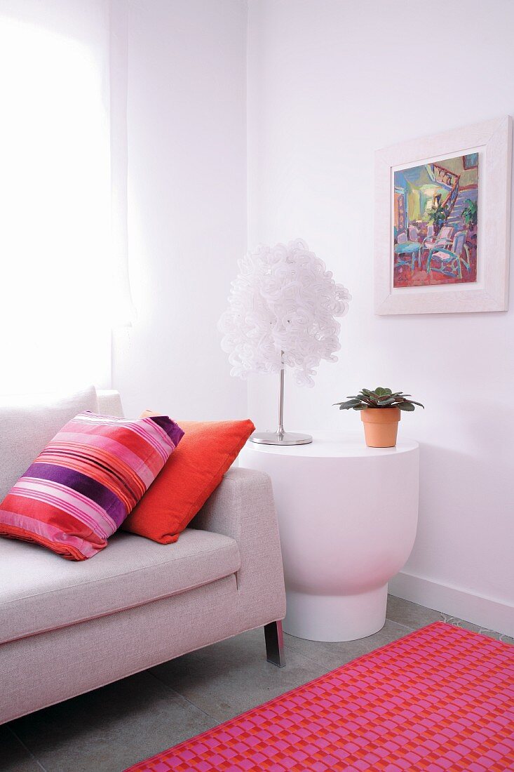 Helles Sofa und weisser Beistelltisch mit Designer Tischlampe, kombiniert mit farbenfrohen Kissen und pinkfarbenem Teppich