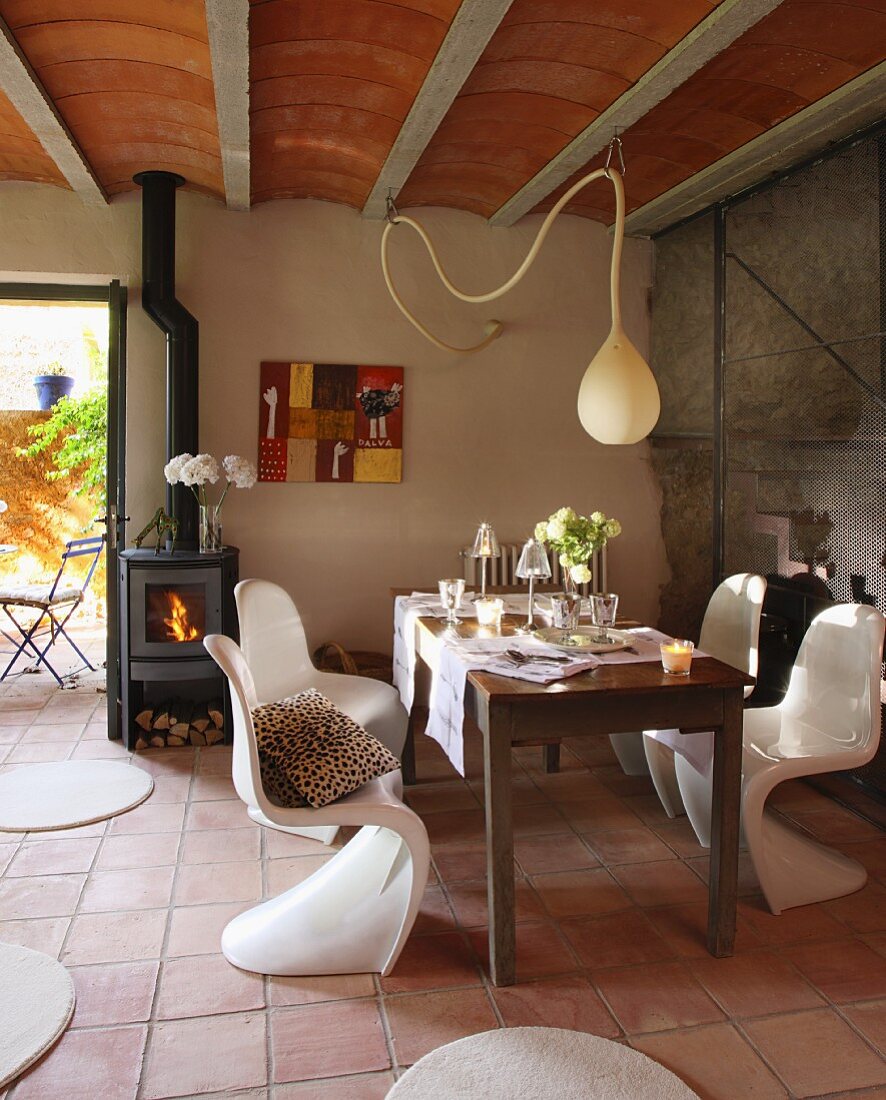 Schlichter Holztisch und weiße Kunststoff Schalenstühle unter tropfenförmiger Hängeleuchte in schlichtem Landhaus mit Rippendecke